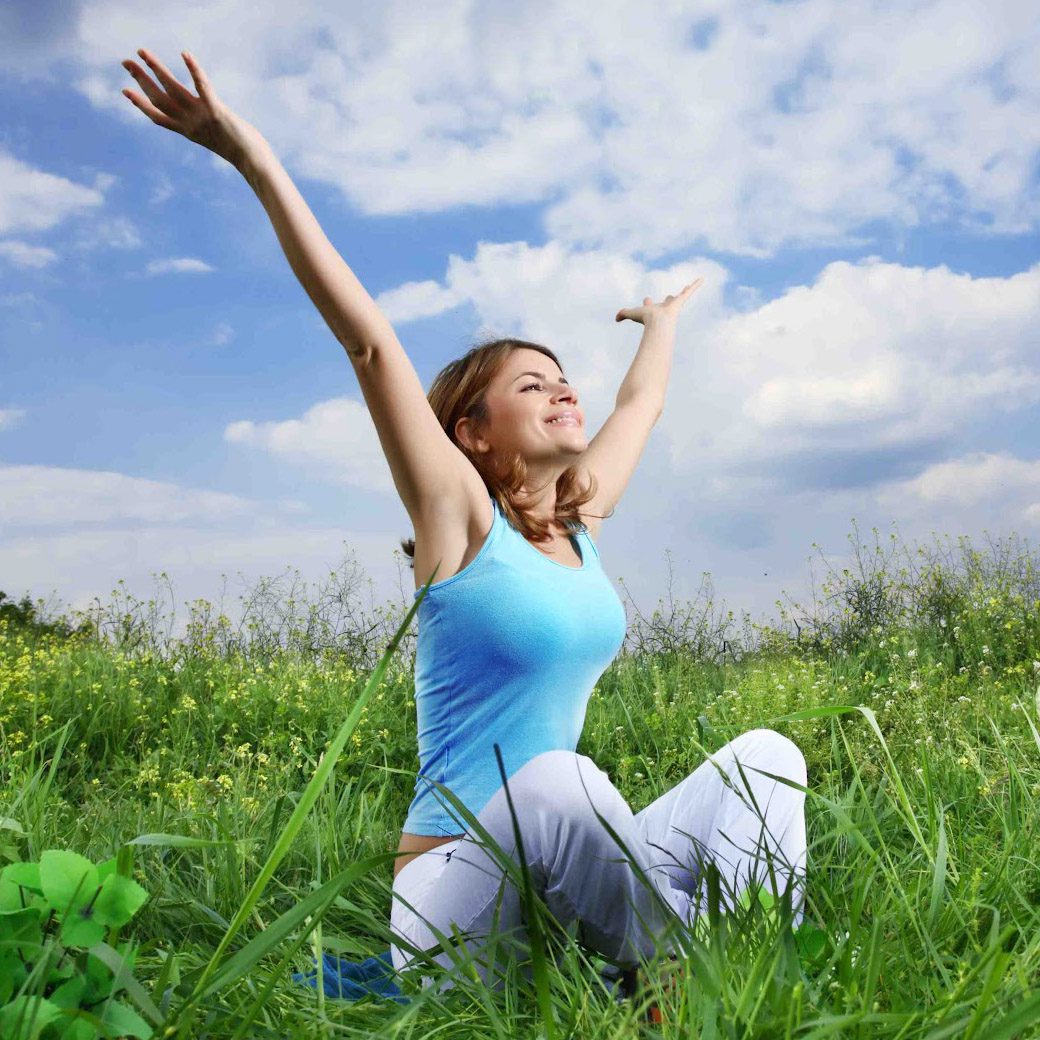 A woman sitting in the grass with her arms raised.