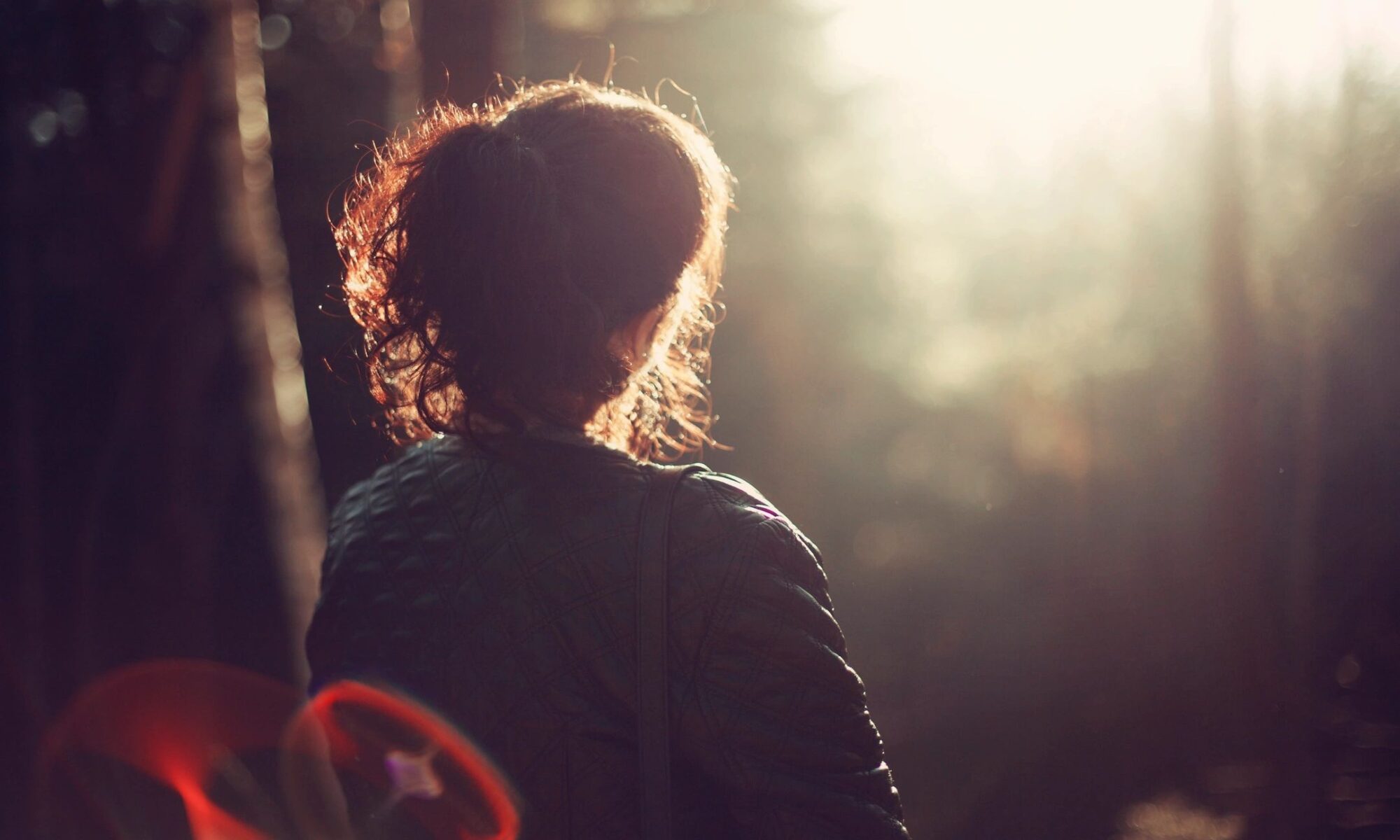 A woman standing in the sunlight near trees.