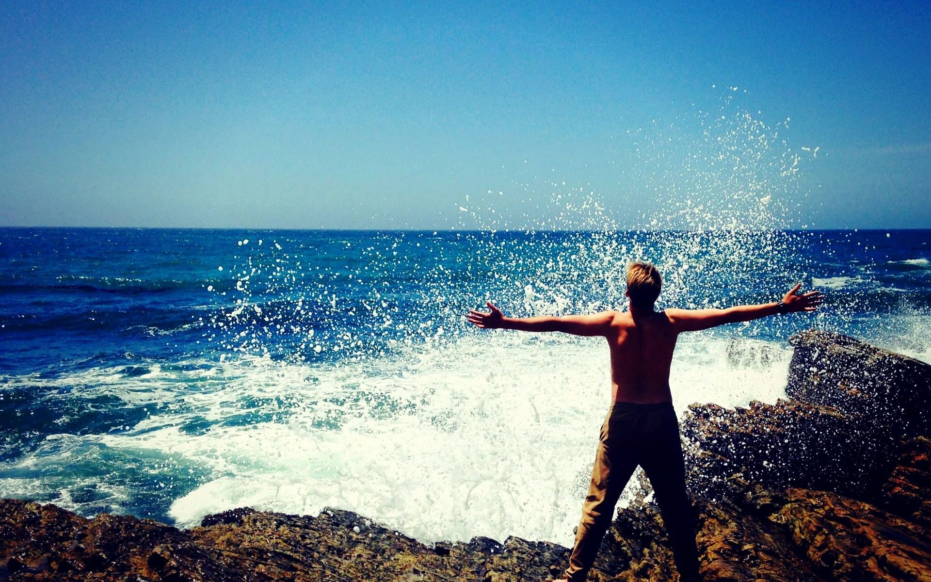 A person standing on top of a rock near the ocean.