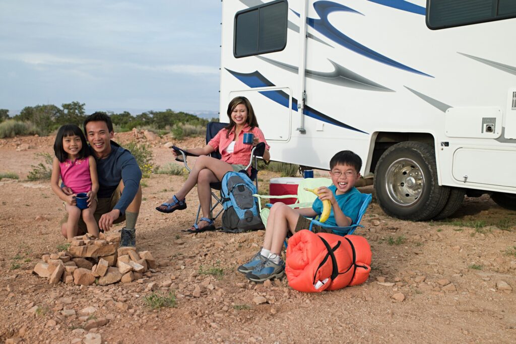 A family sitting on the ground near their rv.