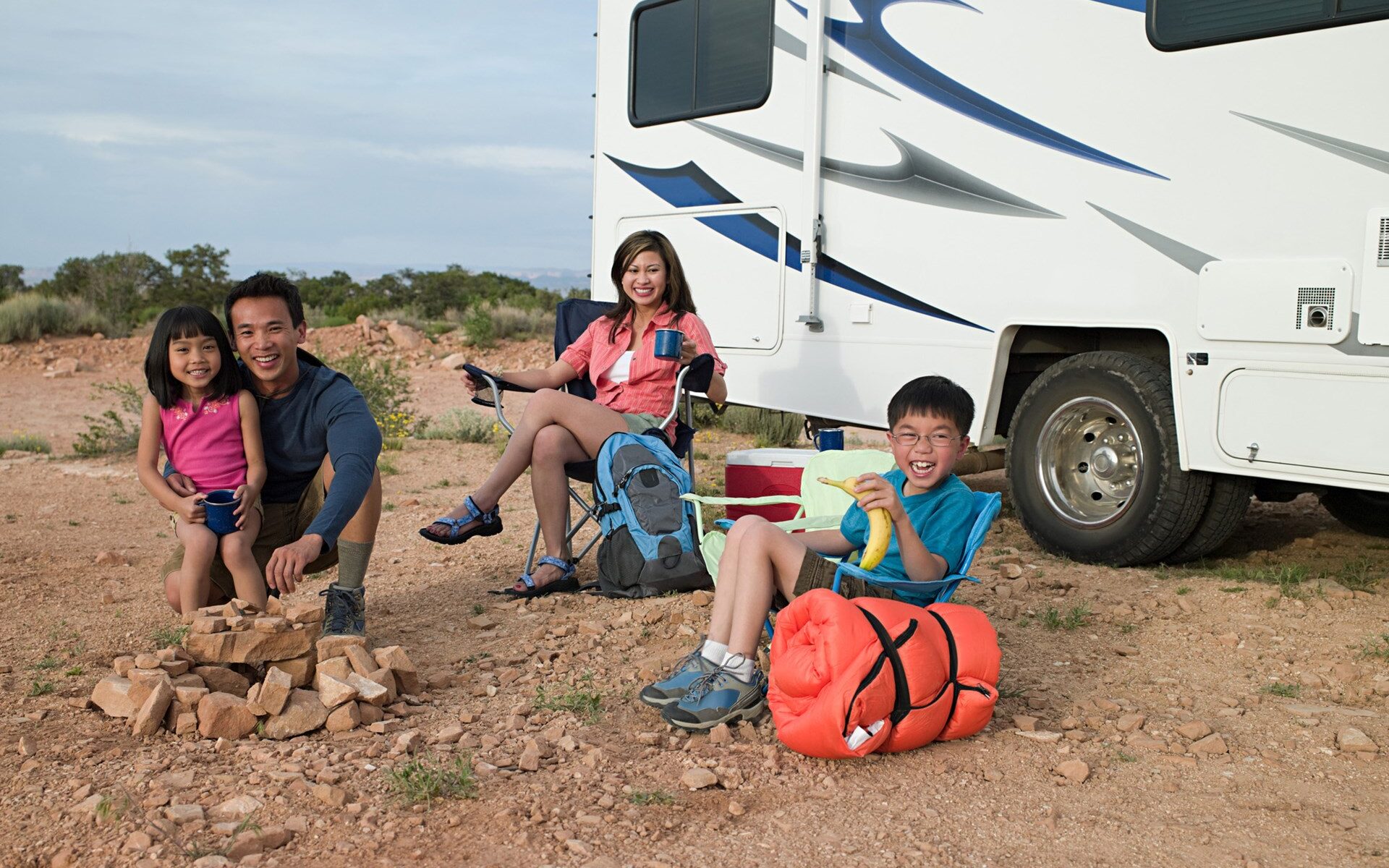 A family sitting on the ground near their rv.