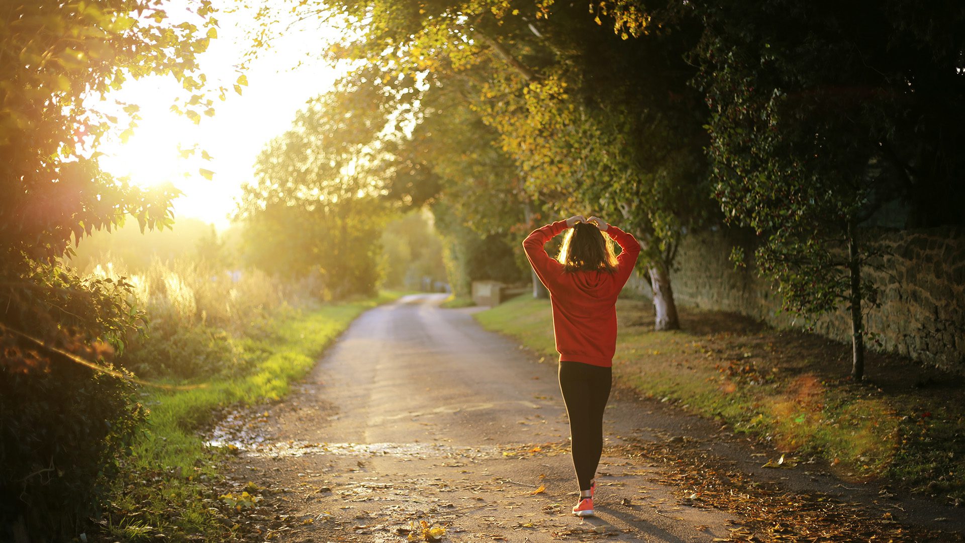 A woman is walking down the road in the sunlight.